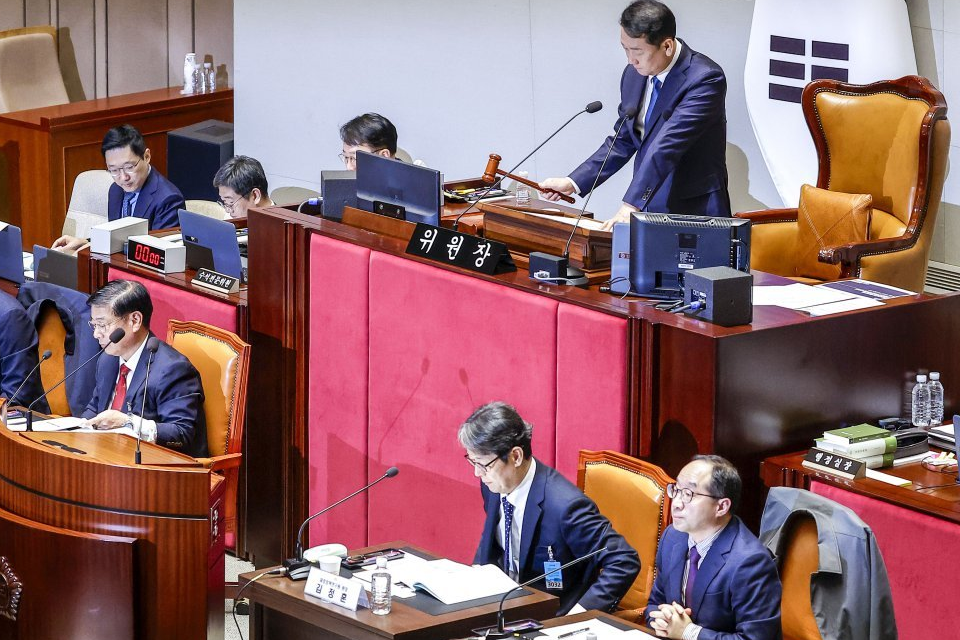 A committee chair holding a gavel and seated participants in a National Assembly meeting room