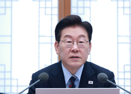 안경과 정장을 착용한 이재명 대통령이 마이크 앞에 앉아 발언하는 모습