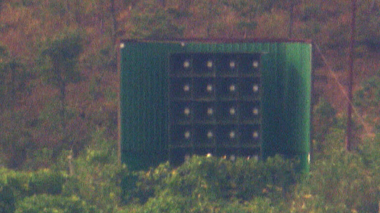 An array of loudspeakers inside a green structure among trees