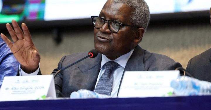 Aliko Dangote gestures with one hand while speaking into a microphone at a meeting.