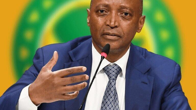 CAF president Patrice Motsepe gestures while speaking into a microphone against a green and yellow backdrop.