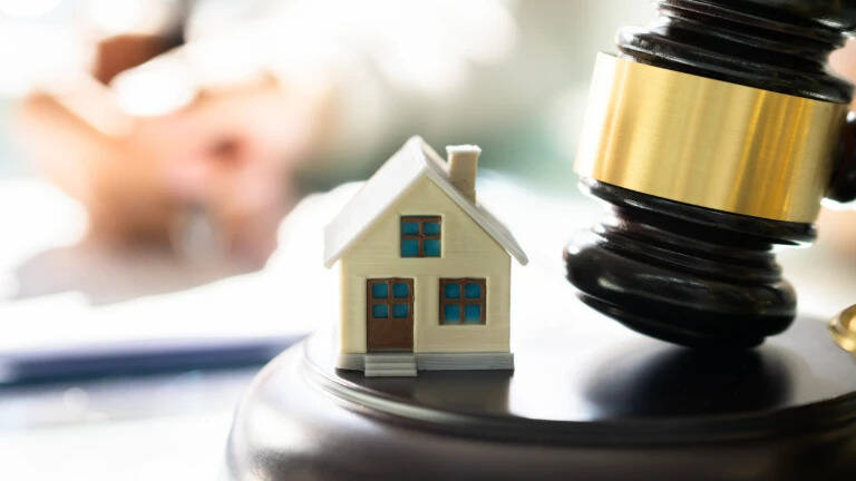 A miniature house beside a wooden gavel on a desk.