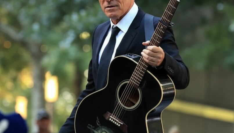 Bruce Springsteen holding a black acoustic guitar outdoors.
