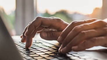 Hands typing on a laptop keyboard beside a window.