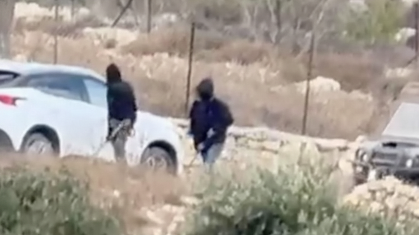 비포장 시골길의 흰색 차량 옆에 두 사람이 서 있고, 근처에 어두운색 차량 일부가 보인다.