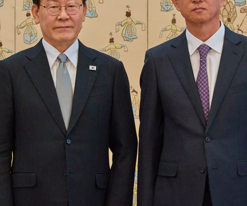 Upper bodies of President Lee Jae-myung and Special Inspector Choi Gil-su standing side by side in front of a folding screen. Parts of both heads are cropped at the top.