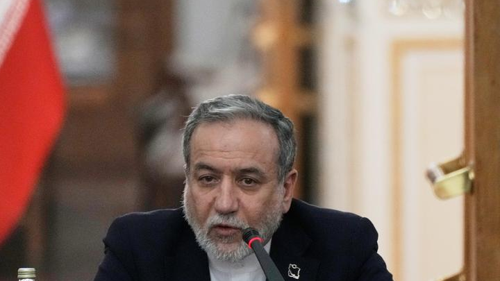 Iranian Foreign Minister Abbas Araghchi seated at a microphone, with part of an Iranian flag visible beside him.
