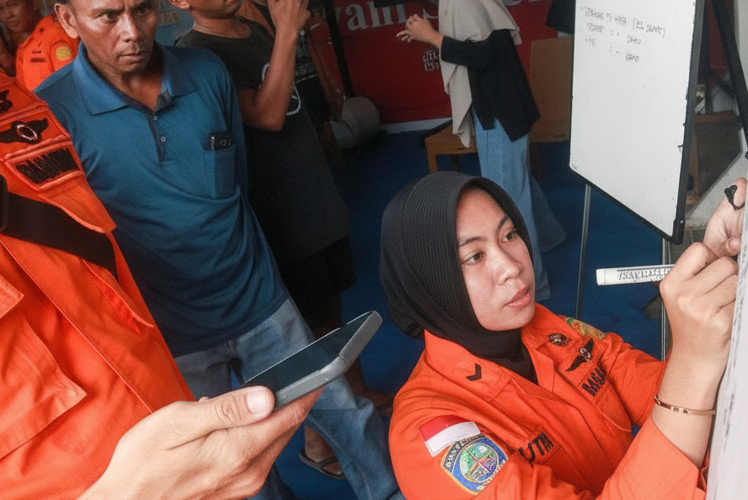 An orange-uniformed rescue officer writes on a whiteboard as people look on.