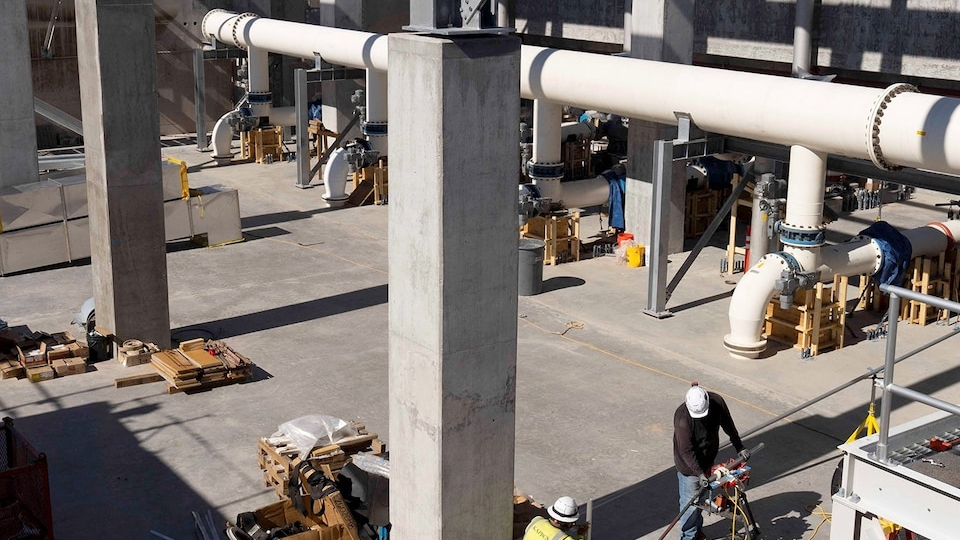 Workers among large pipes, concrete supports and construction materials.