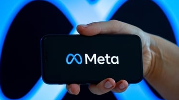 A hand holds a smartphone displaying Meta's name and symbol against a large blue Meta symbol.