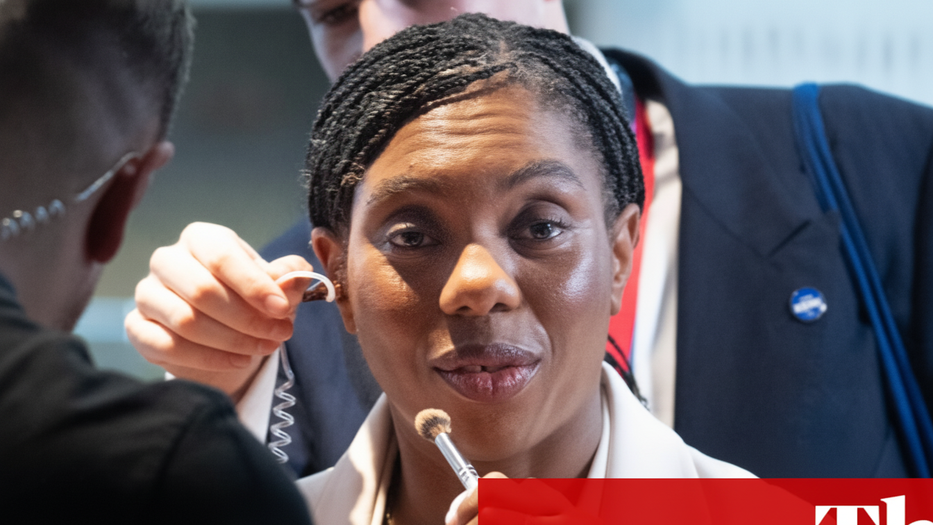 Kemi Badenoch with a makeup brush held near her chin.