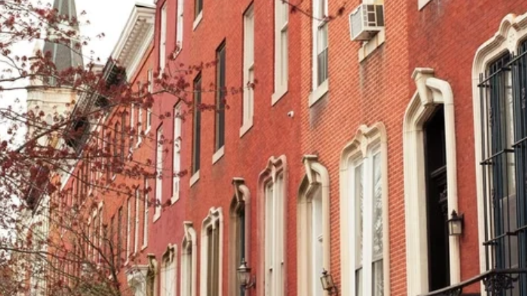 Red-brick row houses with pale window and doorway trim, black railings and tree branches.