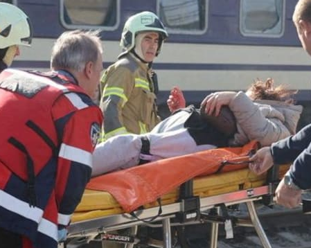 Emergency responders move a person on a stretcher beside a passenger train.