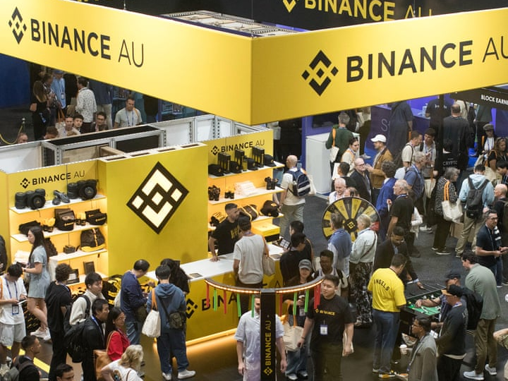 Visitors gather around a Binance AU exhibition booth beneath yellow company signs.