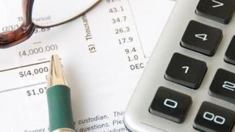 A calculator, eyeglasses and a green pen on financial paperwork.