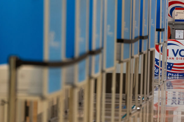 Rows of blue voting booths, with part of a San Diego County voting sign visible at the right edge.