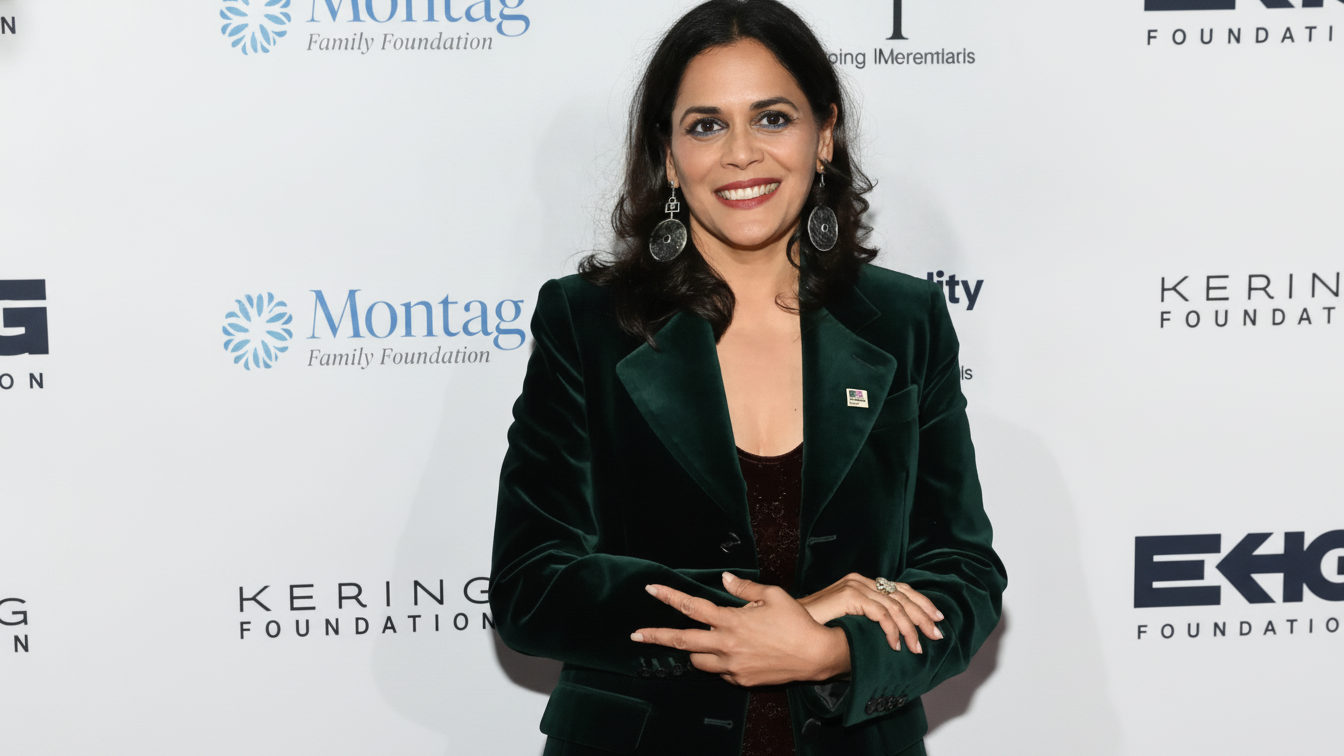 A woman in a dark green jacket smiles in front of a backdrop displaying foundation and Equality Now names.