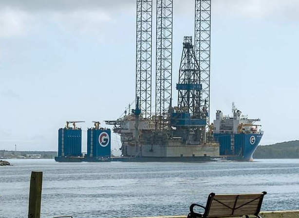 An offshore drilling rig aboard a heavy-lift vessel in Halifax harbour, seen from the waterfront.