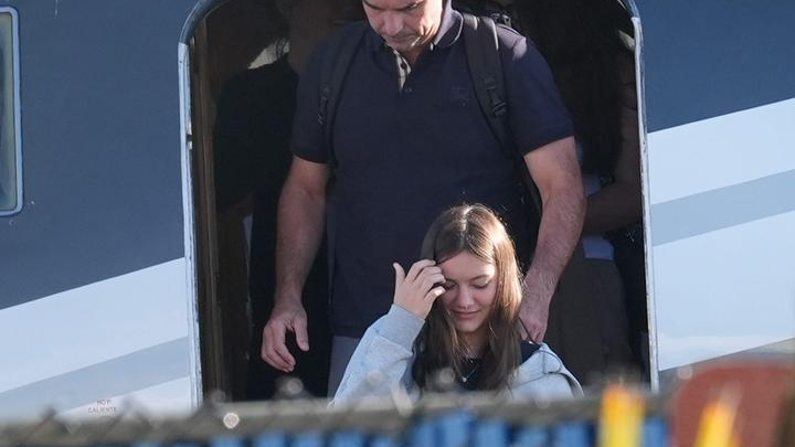 A man stands behind a younger passenger at the open doorway of an aircraft.